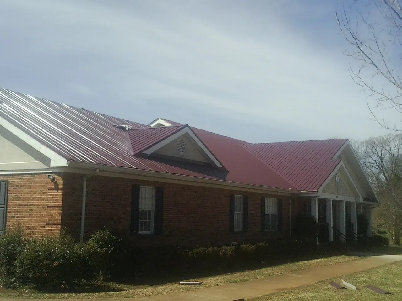 Red metal roof with gabled entries on a long brick building, from a Hail Damage Roof Repair job in Vienna